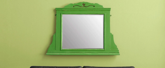 Green mirror with decorative frame hanging above fireplace
