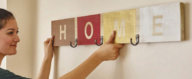 Coat hanger reading "HOME" being hung on the wall by a woman
