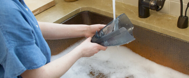 Woman washing vacuum dust bin in kitchen sink