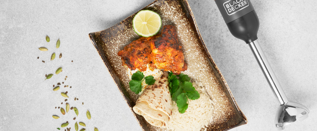 Grey, BLACK+DECKER kitchen wand with immersion blender attachment lying next to a plate of tandoori chicken