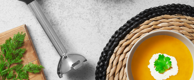 Grey, BLACK+DECKER kitchen wand with immersion blender attachment lying next to a bowl of carrot, orange and ginger soup