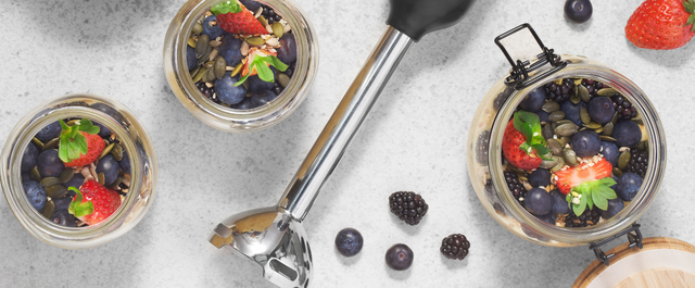 Grey, BLACK+DECKER kitchen wand with immersion blender attachment lying next to a jar of overnight oats, fruit and superfoods
