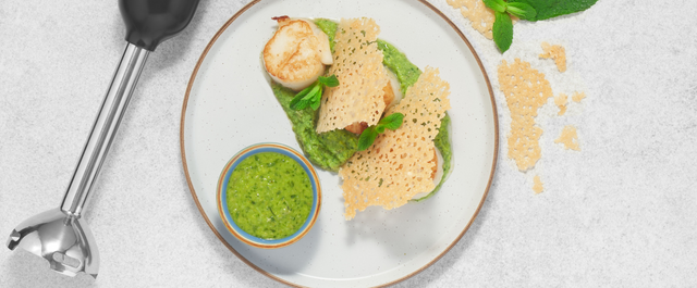 Grey, BLACK+DECKER kitchen wand with immersion blender attachment lying next to a plate of scallops on pea puree
